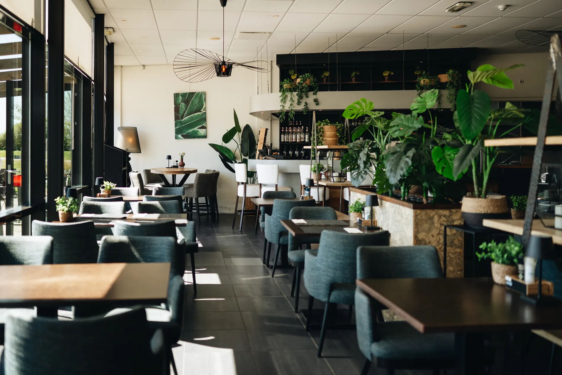 Modern en licht interieur van Restaurant Zeeuws Verlangen met comfortabele groenblauwe stoelen, houten tafels en veel grote, groene kamerplanten die zorgen voor een botanische sfeer.